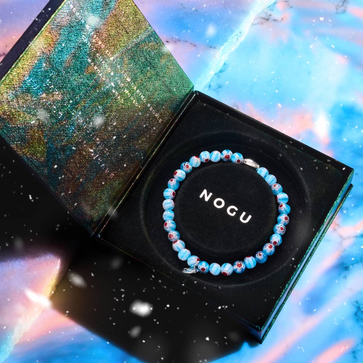 Alpine Bloom Millefiori Bracelet with alpine blue flower beads and sterling silver charm in black NOGU box with iridescent lid